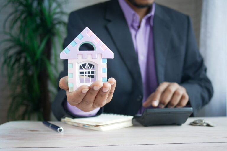 Person holding a model house at a desk with a calculator, representing mortgage calculations